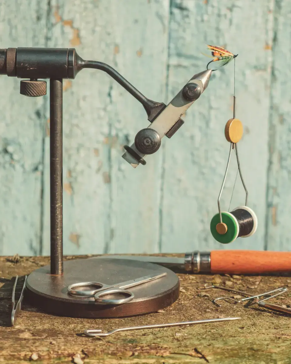 Fly tying vise with materials on a rustic wooden workbench